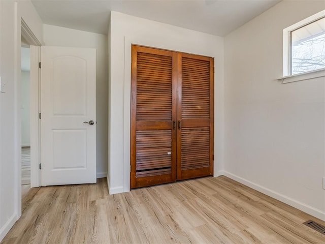 unfurnished bedroom with a closet, visible vents, light wood-style flooring, and baseboards