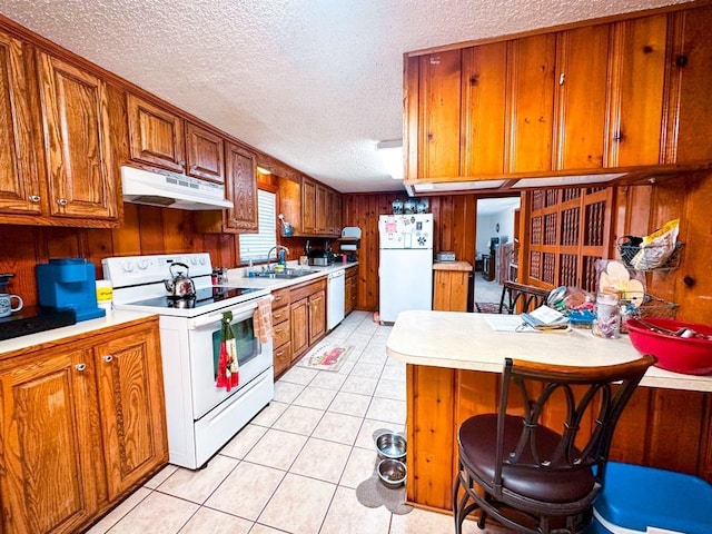 kitchen featuring under cabinet range hood, light countertops, light tile patterned floors, brown cabinets, and white appliances