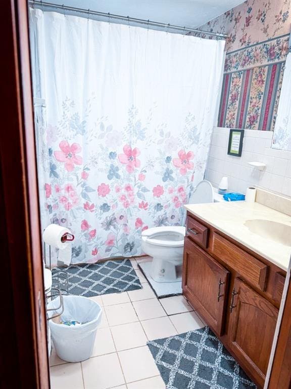 bathroom with vanity, wallpapered walls, tile patterned flooring, tile walls, and toilet