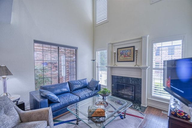 living area with a wealth of natural light, a towering ceiling, wood finished floors, and a high end fireplace