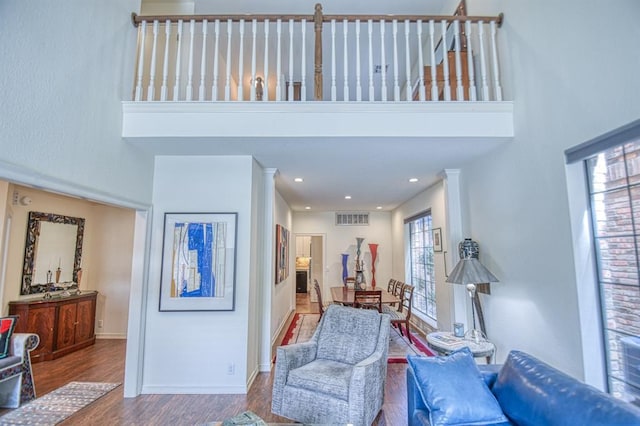 living area with visible vents, baseboards, wood finished floors, and a towering ceiling