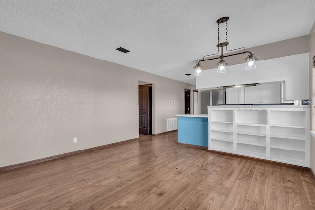 kitchen featuring visible vents, baseboards, pendant lighting, wood finished floors, and a textured ceiling