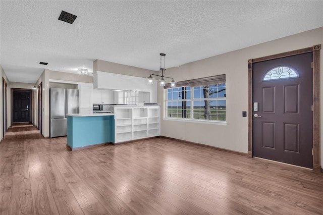 kitchen with a wealth of natural light, white cabinets, freestanding refrigerator, and wood finished floors