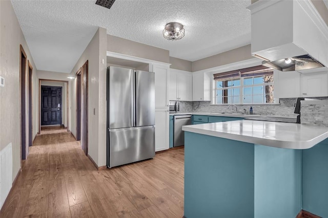 kitchen featuring stainless steel appliances, a peninsula, wall chimney exhaust hood, white cabinets, and light wood finished floors