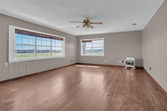 empty room with visible vents, ceiling fan, hardwood / wood-style floors, heating unit, and a textured ceiling