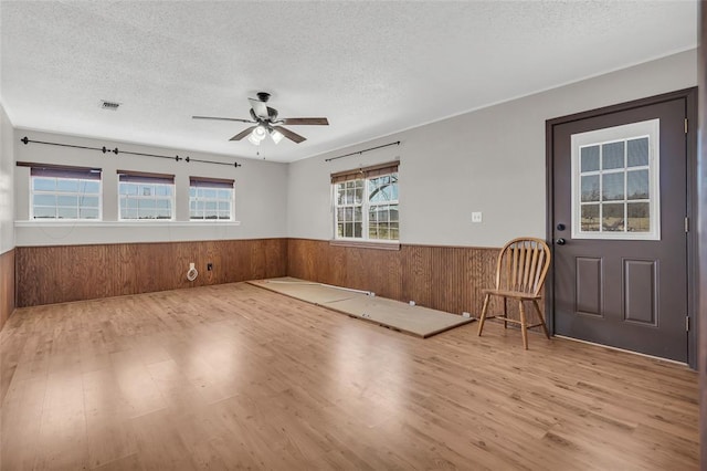 empty room featuring wooden walls, wainscoting, and a textured ceiling