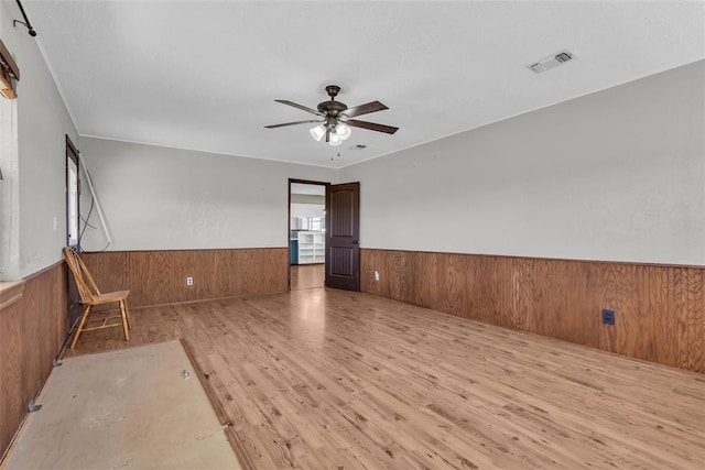 unfurnished room featuring visible vents, wooden walls, a wainscoted wall, wood finished floors, and a ceiling fan