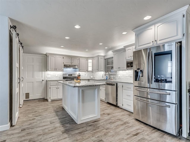 4303 N Redmond Ave, Bethany, OK 73008 - kitchen with stainless steel appliances, under cabinet range hood, backsplash, light stone counters, and a center island