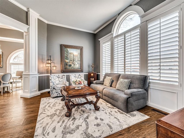 living area with ornamental molding, decorative columns, wainscoting, wood finished floors, and a decorative wall