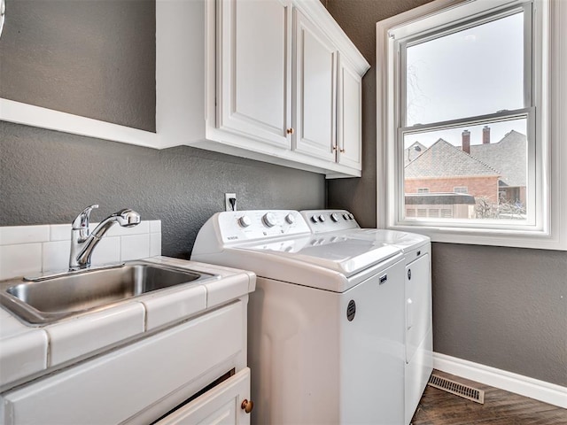 washroom featuring visible vents, a sink, washing machine and dryer, cabinet space, and a textured wall