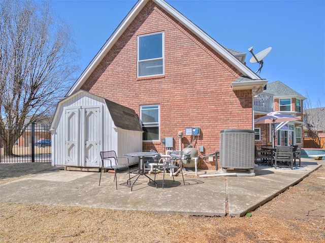 back of property featuring a storage unit, an outbuilding, fence, brick siding, and a patio area