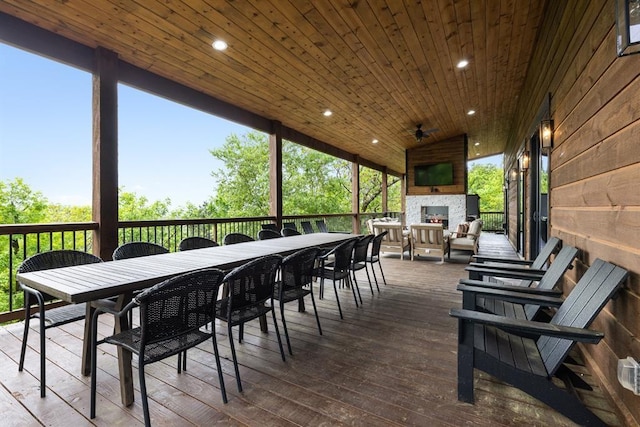 wooden terrace featuring an outdoor stone fireplace and outdoor dining space