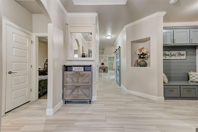 hallway with a barn door, arched walkways, baseboards, and ornamental molding