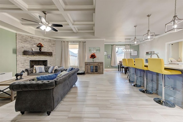 living room featuring ornamental molding, beam ceiling, a stone fireplace, coffered ceiling, and a ceiling fan