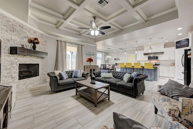 living room featuring visible vents, coffered ceiling, ornamental molding, a stone fireplace, and beamed ceiling