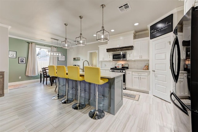 kitchen with a kitchen bar, visible vents, a kitchen island with sink, backsplash, and stainless steel appliances