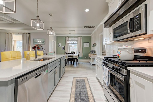 kitchen featuring a sink, stainless steel appliances, light countertops, crown molding, and backsplash