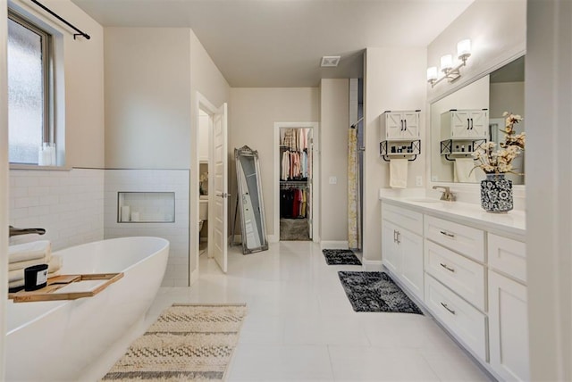 bathroom featuring vanity, tile walls, a fireplace, a soaking tub, and a spacious closet