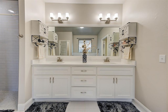 bathroom featuring double vanity, tiled shower, baseboards, and a sink