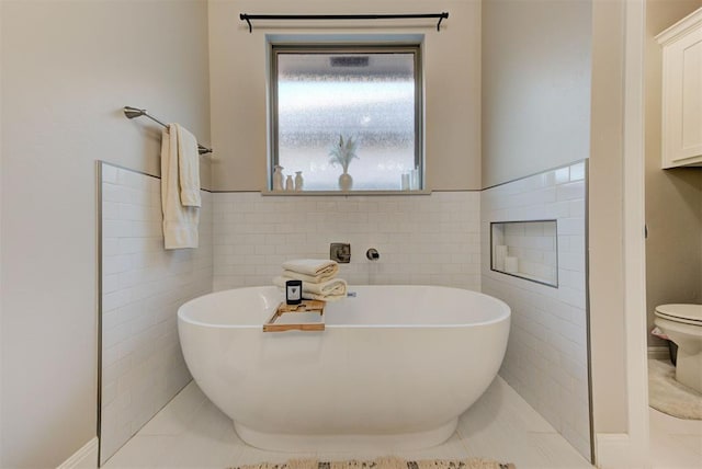 bathroom with toilet, tile walls, a freestanding bath, and tile patterned flooring