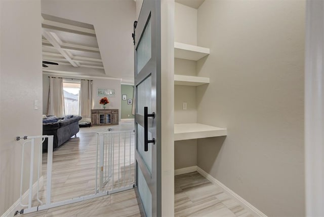 interior space featuring a barn door, baseboards, coffered ceiling, and beam ceiling