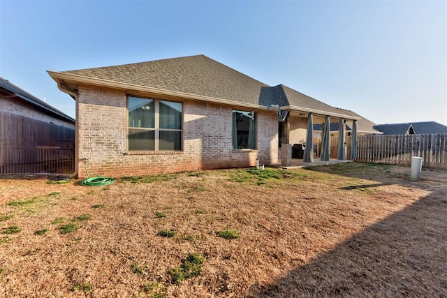 rear view of house with a patio area, brick siding, roof with shingles, and fence