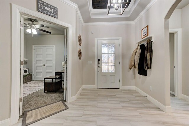 foyer entrance featuring baseboards, ornamental molding, arched walkways, a raised ceiling, and a ceiling fan
