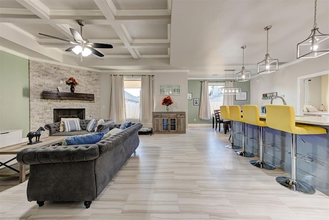 living room featuring coffered ceiling, a fireplace, crown molding, and a ceiling fan