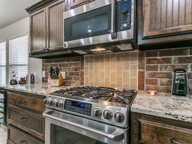 kitchen with dark brown cabinetry, light stone counters, backsplash, and stainless steel appliances