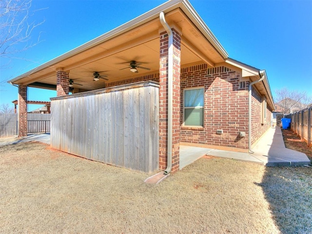 view of home's exterior featuring brick siding, ceiling fan, and fence