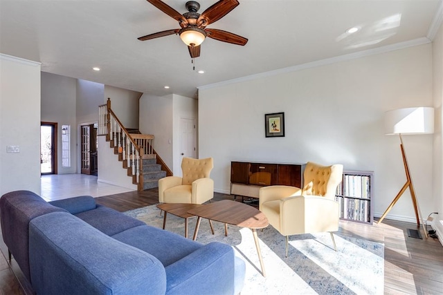 living area with stairway, a ceiling fan, wood finished floors, baseboards, and crown molding