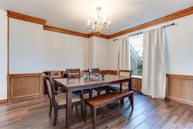 dining space featuring dark wood finished floors, a notable chandelier, a wainscoted wall, and ornamental molding