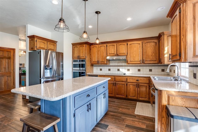 kitchen with a center island, under cabinet range hood, brown cabinetry, stainless steel appliances, and a sink