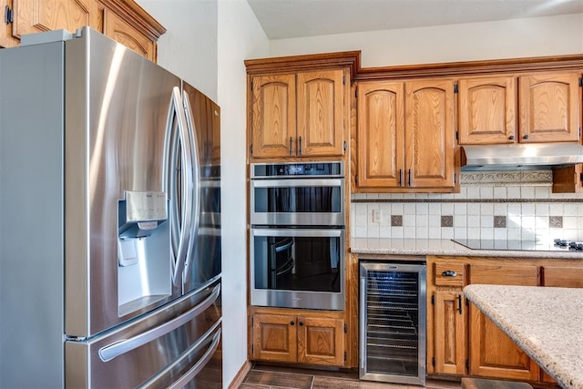 kitchen with brown cabinets, beverage cooler, under cabinet range hood, stainless steel appliances, and decorative backsplash