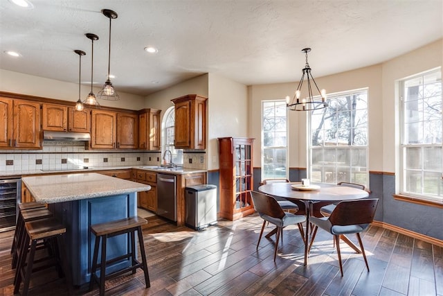 kitchen with under cabinet range hood, black electric cooktop, brown cabinets, and dishwasher