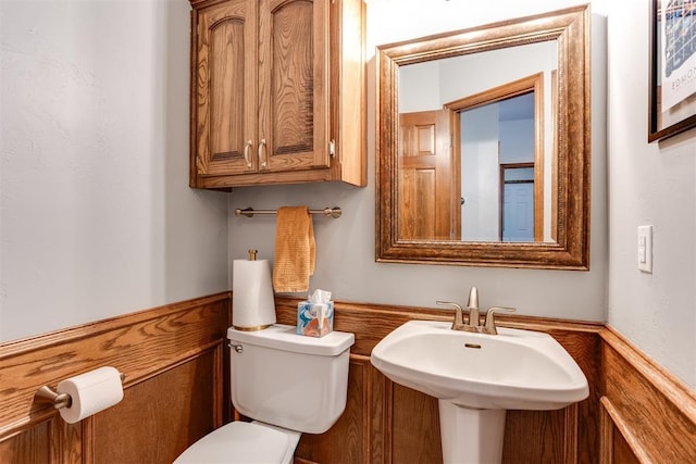 half bath featuring a wainscoted wall, toilet, and a sink