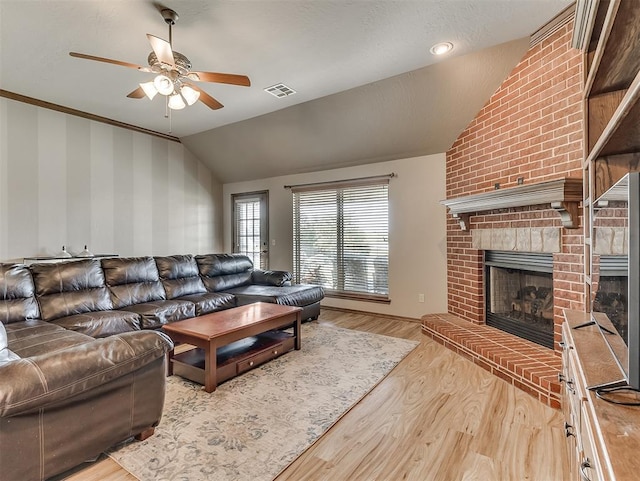 living area featuring visible vents, a brick fireplace, vaulted ceiling, wood finished floors, and a ceiling fan