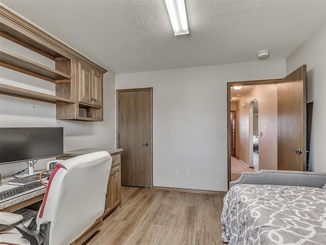 bedroom with baseboards, a textured ceiling, light wood-style flooring, and arched walkways