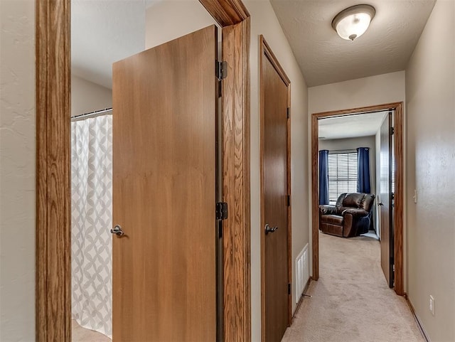 corridor with baseboards, light colored carpet, visible vents, and a textured ceiling