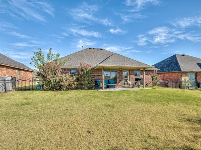 rear view of property featuring brick siding, fence, a lawn, a patio area, and a gate