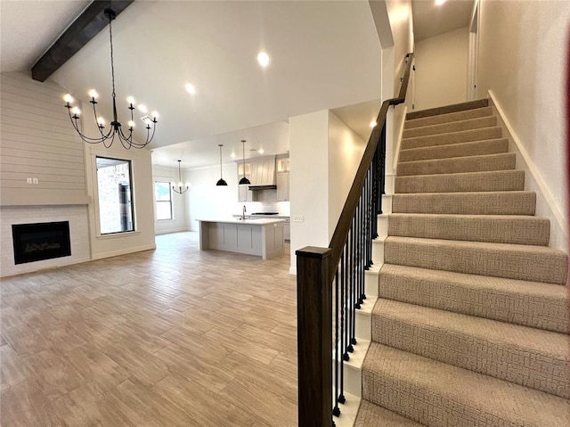 staircase featuring lofted ceiling with beams, wood finished floors, an inviting chandelier, a fireplace, and baseboards