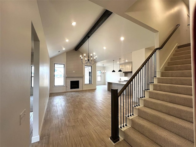 unfurnished living room featuring light wood-style flooring, vaulted ceiling with beams, a sink, stairs, and a large fireplace