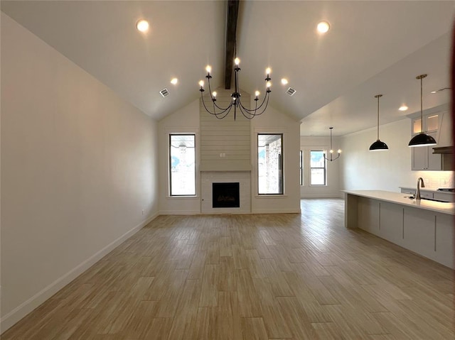 unfurnished living room with a sink, an inviting chandelier, light wood-style flooring, and a fireplace