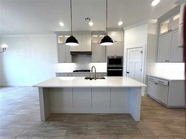 kitchen with tasteful backsplash, an island with sink, light countertops, black appliances, and a sink