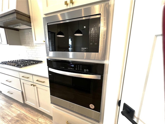 kitchen with light wood-style flooring, tasteful backsplash, ventilation hood, stainless steel appliances, and light countertops