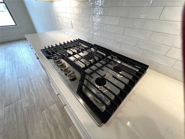 interior details with backsplash, wood finished floors, light countertops, and stainless steel gas stovetop