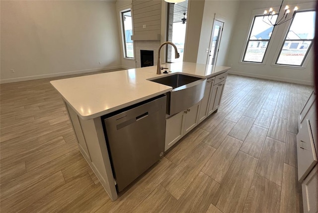 kitchen featuring open floor plan, dishwasher, light countertops, a fireplace, and a sink