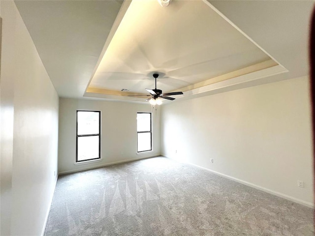 carpeted empty room featuring a tray ceiling, baseboards, and a ceiling fan