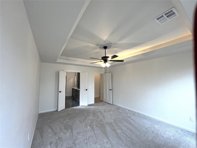 unfurnished bedroom with a raised ceiling, baseboards, visible vents, and carpet floors