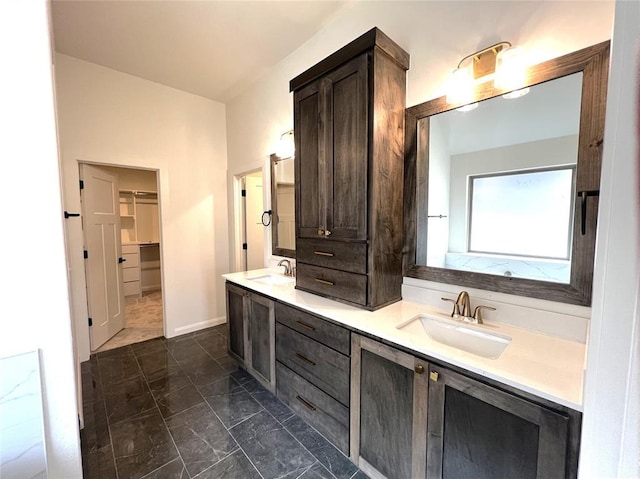 full bath with double vanity, marble finish floor, a walk in closet, and a sink